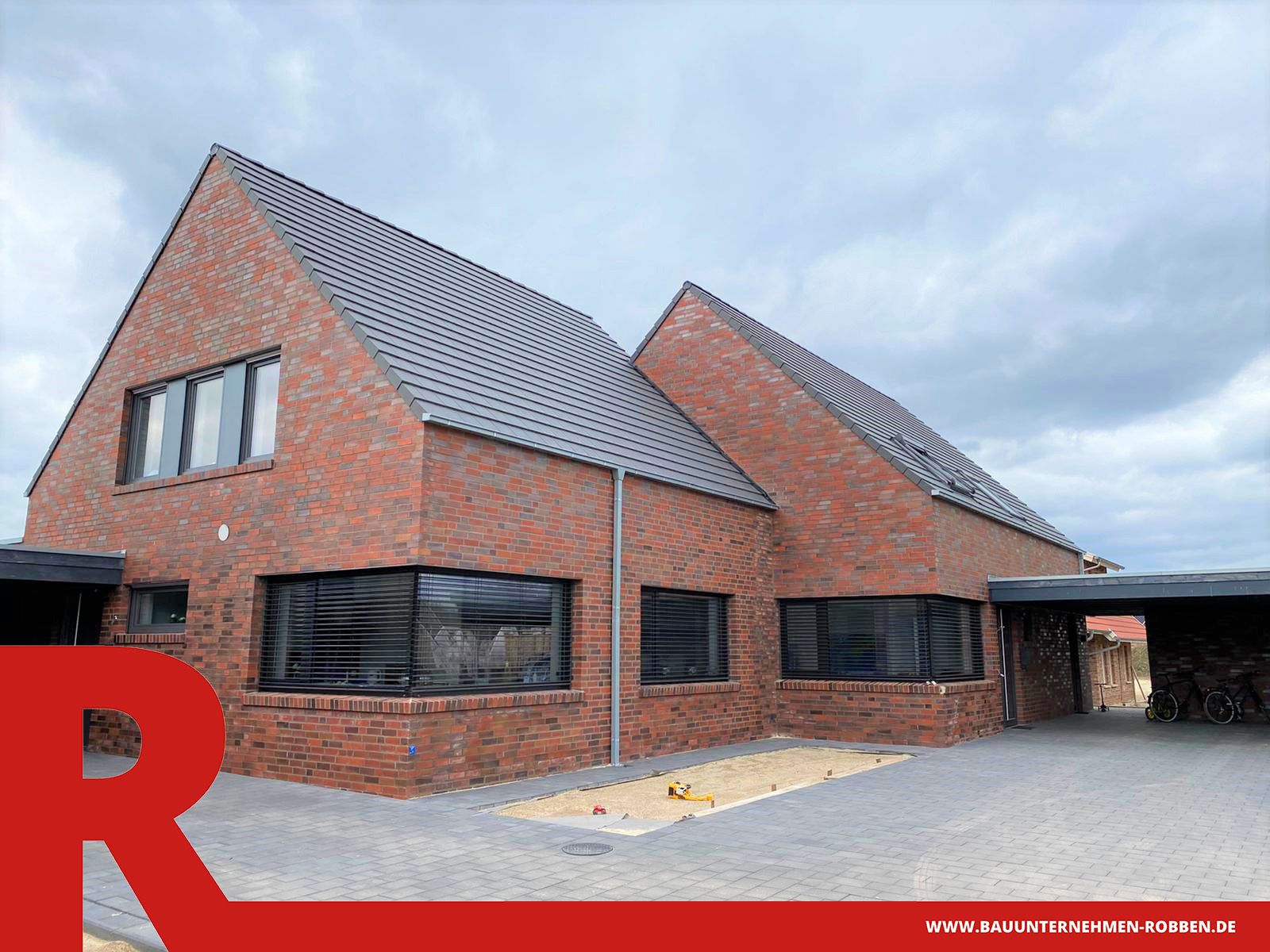 Doppelhaus aus hellrotem Klinker, dunklen Dachziegeln, zwei Carports und gepflasterter Auffahrt.