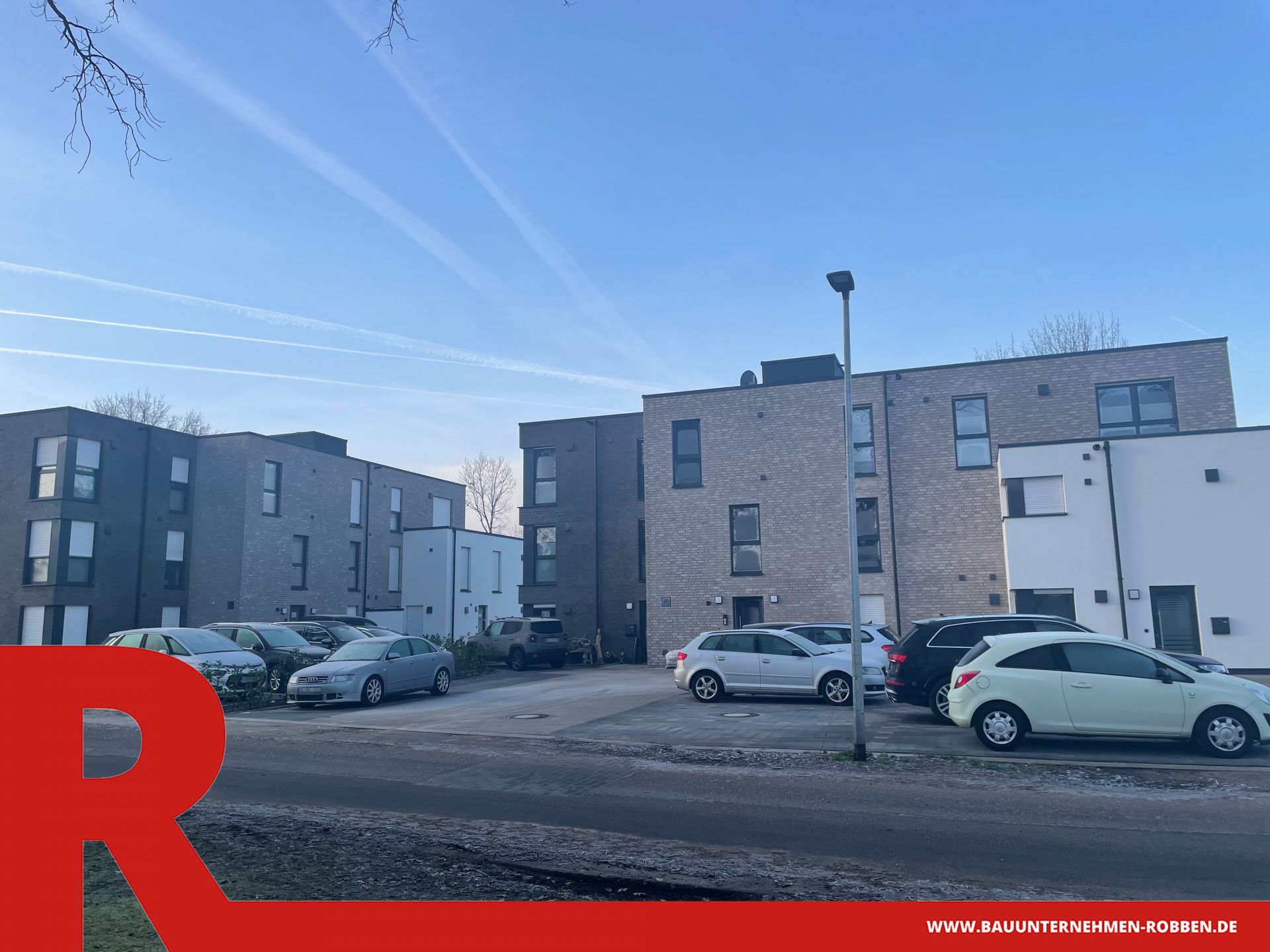 2 Mehrfamilienhäuser in Haselünne Zwei Mehrfamilienhäuser mit verschiedenfarbigen Außenfassaden und Parkplätzen davor.