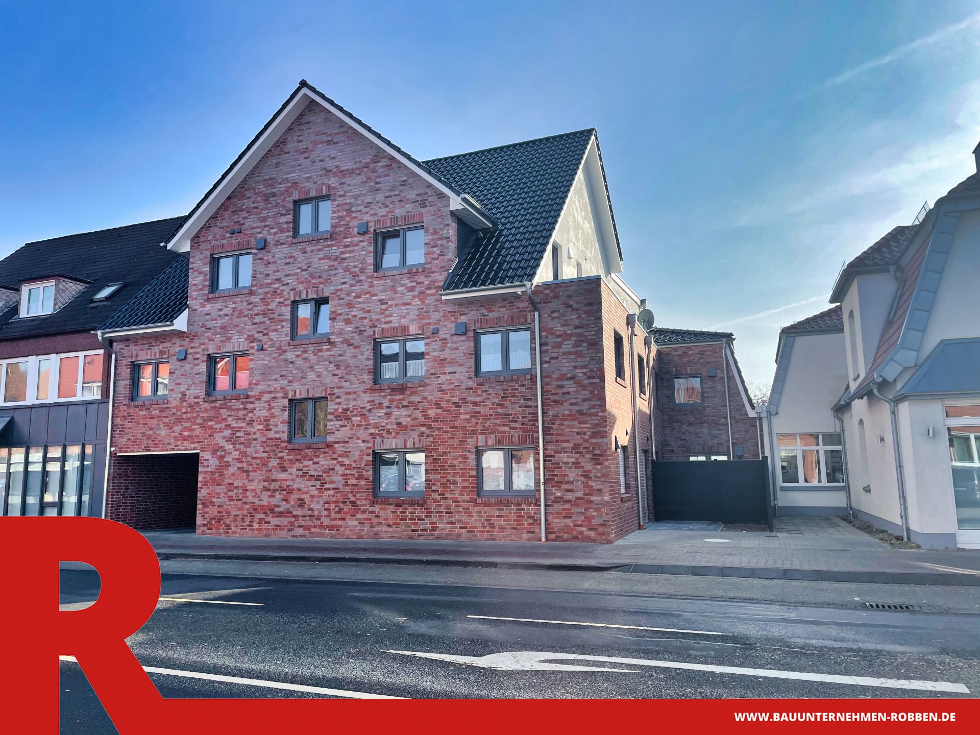 Mehrfamilienhaus in Meppen 2 Ein Mehrfamilienhaus mit roten Klinkern, blauen Dachziegeln und mehreren Parkplätzen.