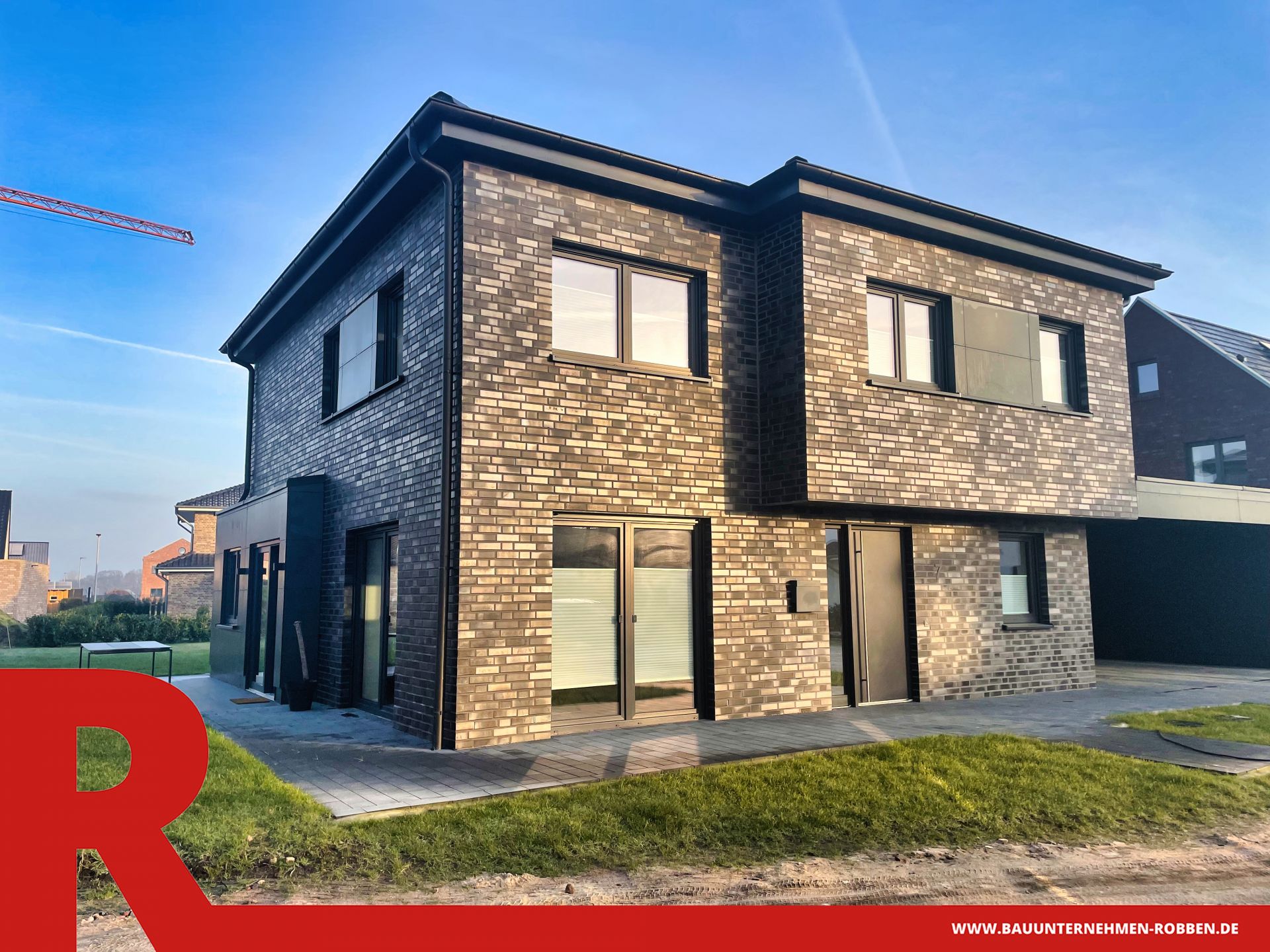 Einfamilienhaus in Haselünne 1 Modernes Zweifamilienhaus mit dunklen Ziegeln, großen Fenstern und Carport.