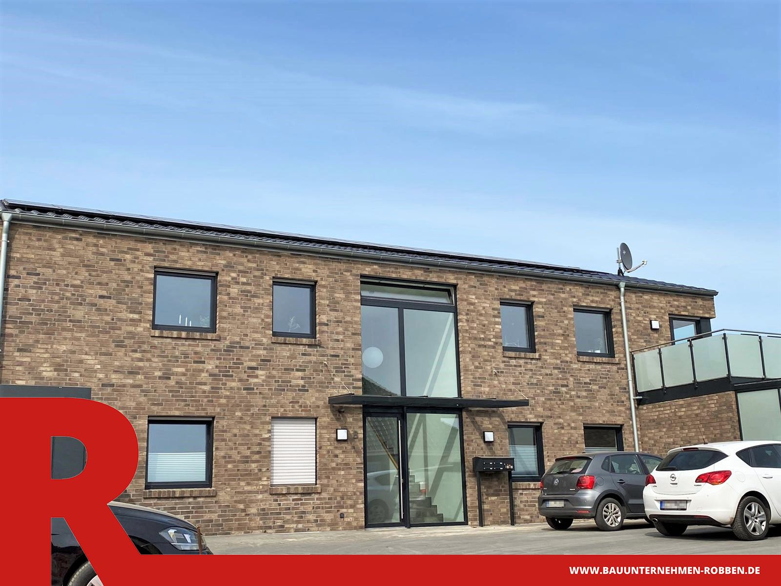 Mehrfamilienhaus mit 5 Wohneinheiten Mehrfamilienhaus aus hellrotem Klinker, mit einer großen Fensterfront am Eingang und einem Balkon.