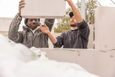 Zwei Maurer heben einen Block für einen Rohbau.