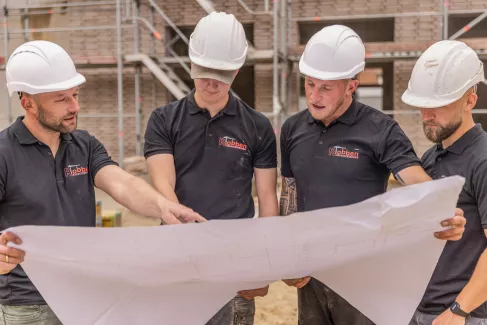 Vier Maurer schauen auf eine Bauzeichnung.