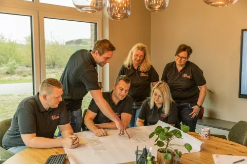 Nico Robben erklärt den Mitarbeitern etwas auf einem Bauplan, der auf einem Tisch liegt.