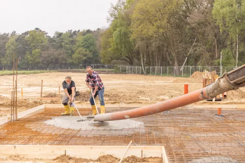 Zwei Maurer ziehen Beton für ein neues Fundament.