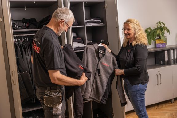 Die Personalerin zeigt einem Bauleiter die Betriebskleidung.