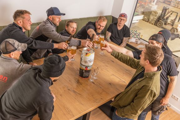 Impression_20 Zehn Mitarbeiter stoßen im Aufenthaltsraum der Mitarbeiter an.