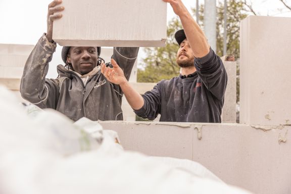 Zwei Maurer heben einen Block f&uuml;r einen Rohbau.