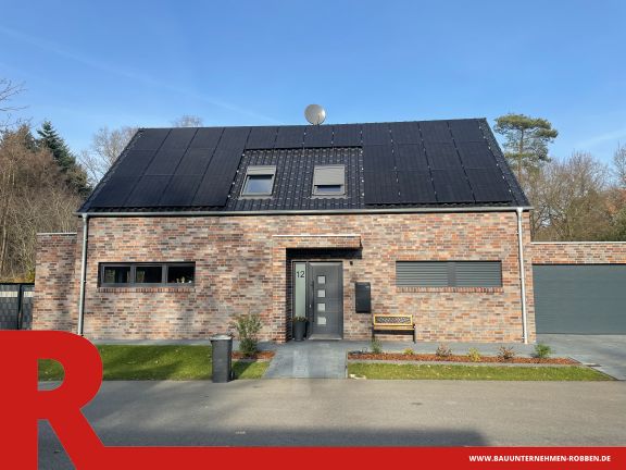 Einfamilienhaus mit hellrotem Klinker, blauen Dachziegeln, Doppelgarage und PV-Anlagen.