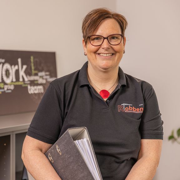 Anke Byl Foto der Buchhalterin Anke Byl mit einem Aktenordner unter dem Arm.