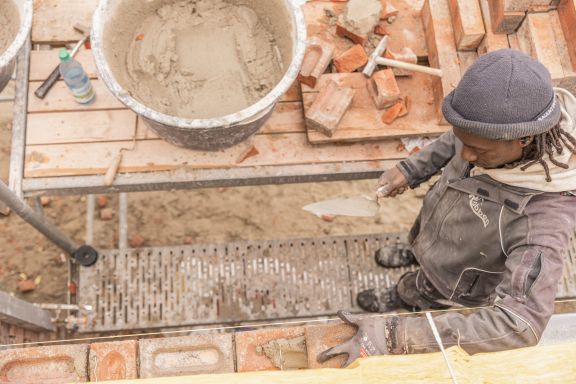 Aufnahme eines Maurers, der einen Stein auf eine Mauer legt, aus der Vogelperspektive.
