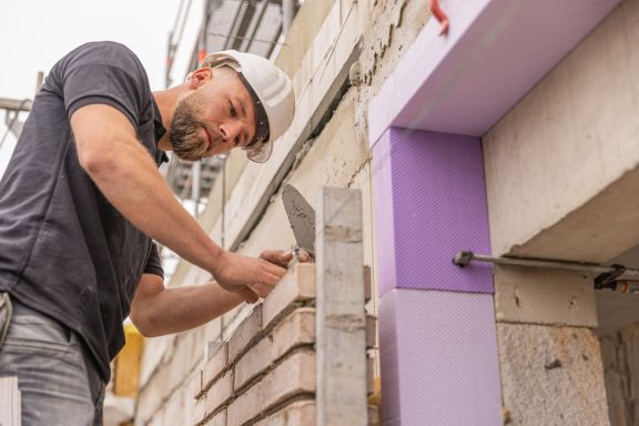 Maurerarbeiten Ein Mitarbeiter verlegt einen neuen Stein auf eine Mauer.