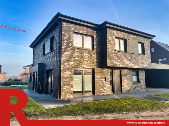 Einfamilienhaus in Haselünne 1 Modernes Zweifamilienhaus mit dunklen Ziegeln, großen Fenstern und Carport.