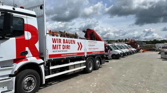 Lagerplatz auf dem vorne links ein LKW mit gro&szlig;er Ladefl&auml;che und Kran steht.