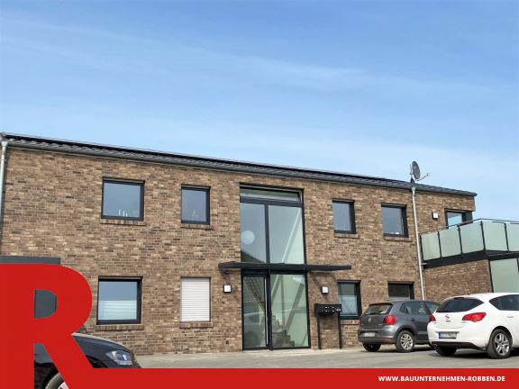 Mehrfamilienhaus mit 5 Wohneinheiten Mehrfamilienhaus aus hellrotem Klinker, mit einer großen Fensterfront am Eingang und einem Balkon.