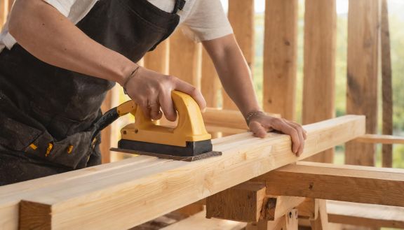 Schleifen eines Holzbalkens Ein Zimmerer schleift einen Holzbalken für den Bau eines Daches.