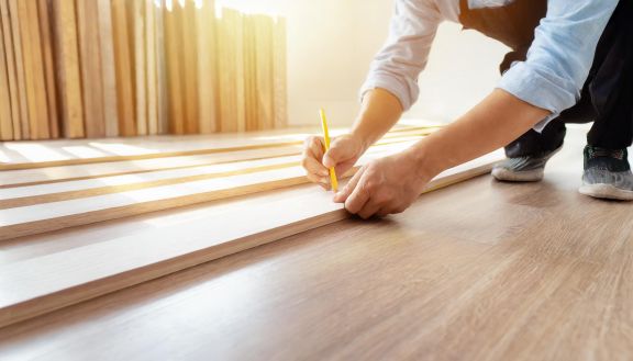 Innenausbau eines Wohnraumes Ein Mann vermisst eine Holzleiste zur Verlegung eines Fußbodens in einem Innenraum.